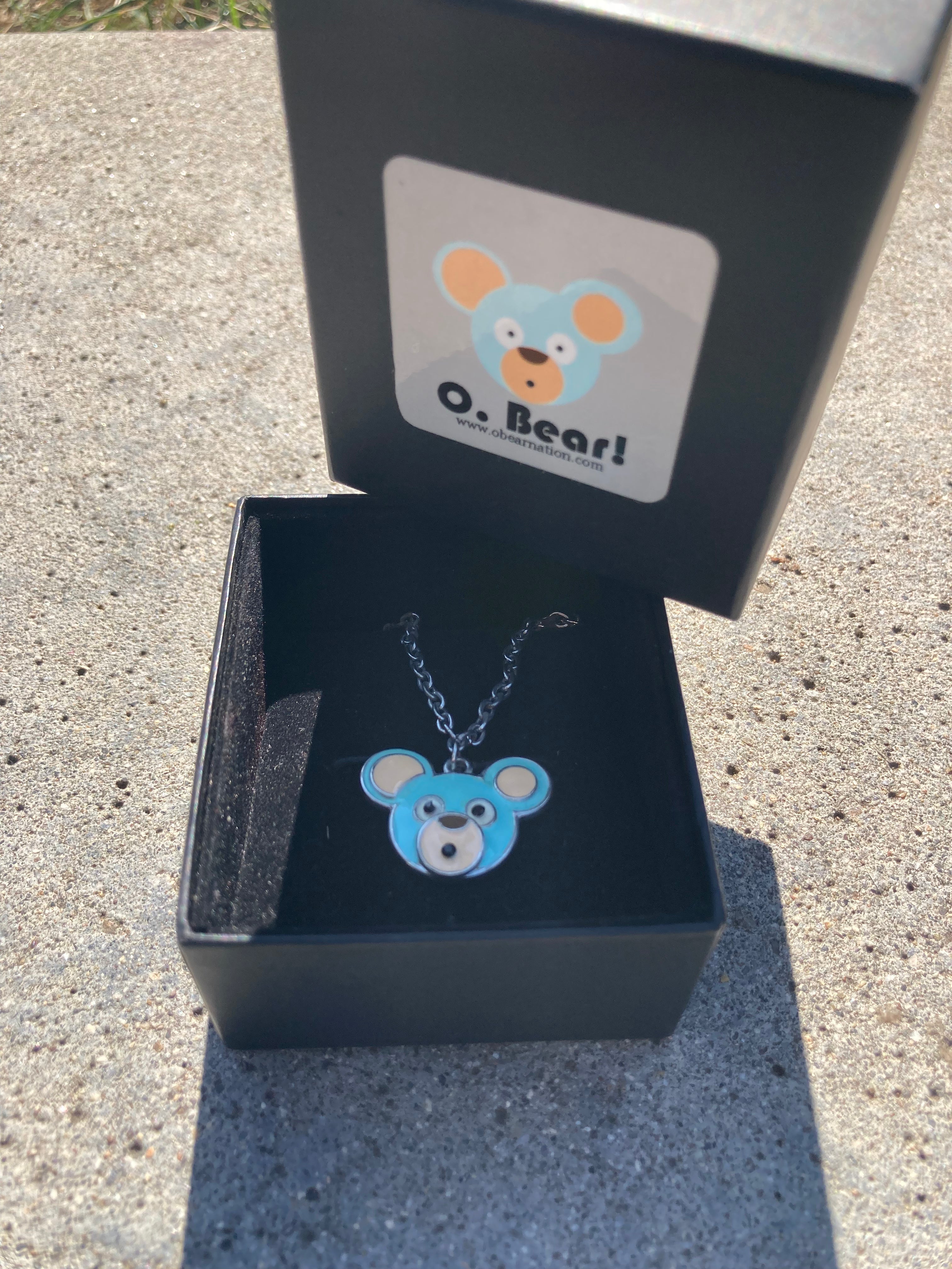 Blue bear-shaped necklace in an open black box with a visible brand logo.