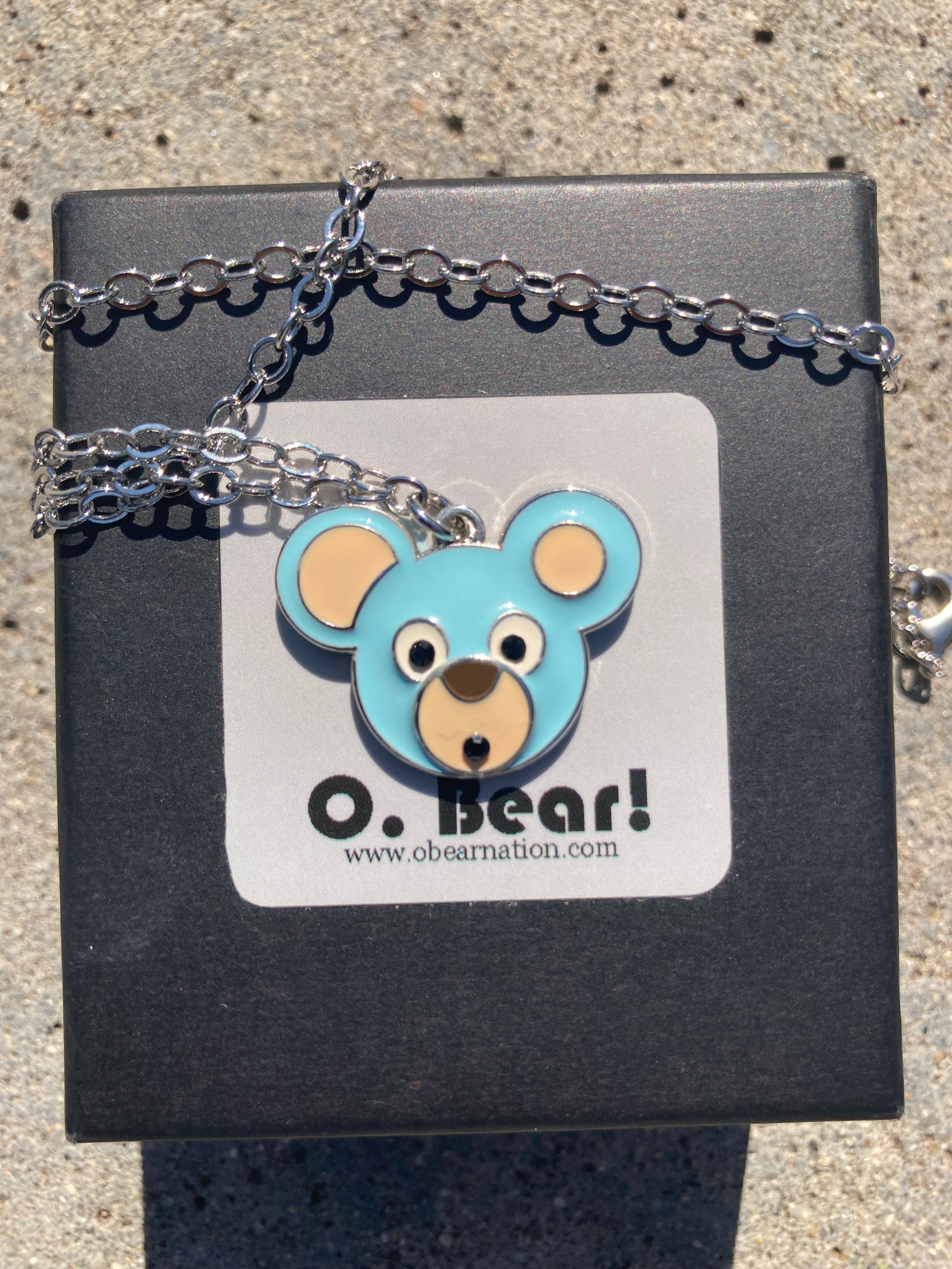 Necklace with a blue bear pendant on a black box labeled 'O. Bear!'.
