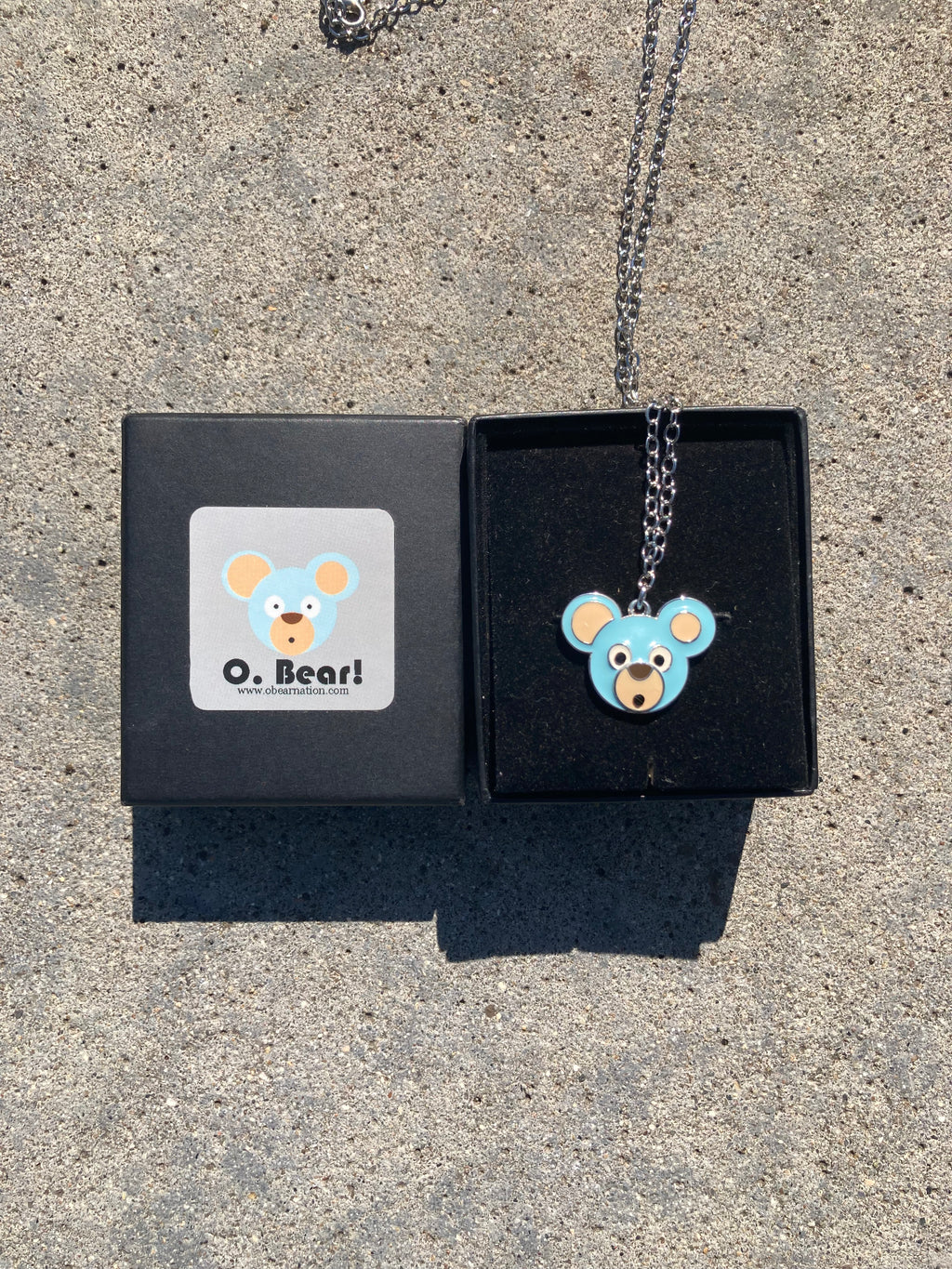 Necklace with an O. Bear pendant in a black box on a concrete surface