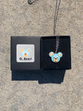 Necklace with an O. Bear pendant in a black box on a concrete surface
