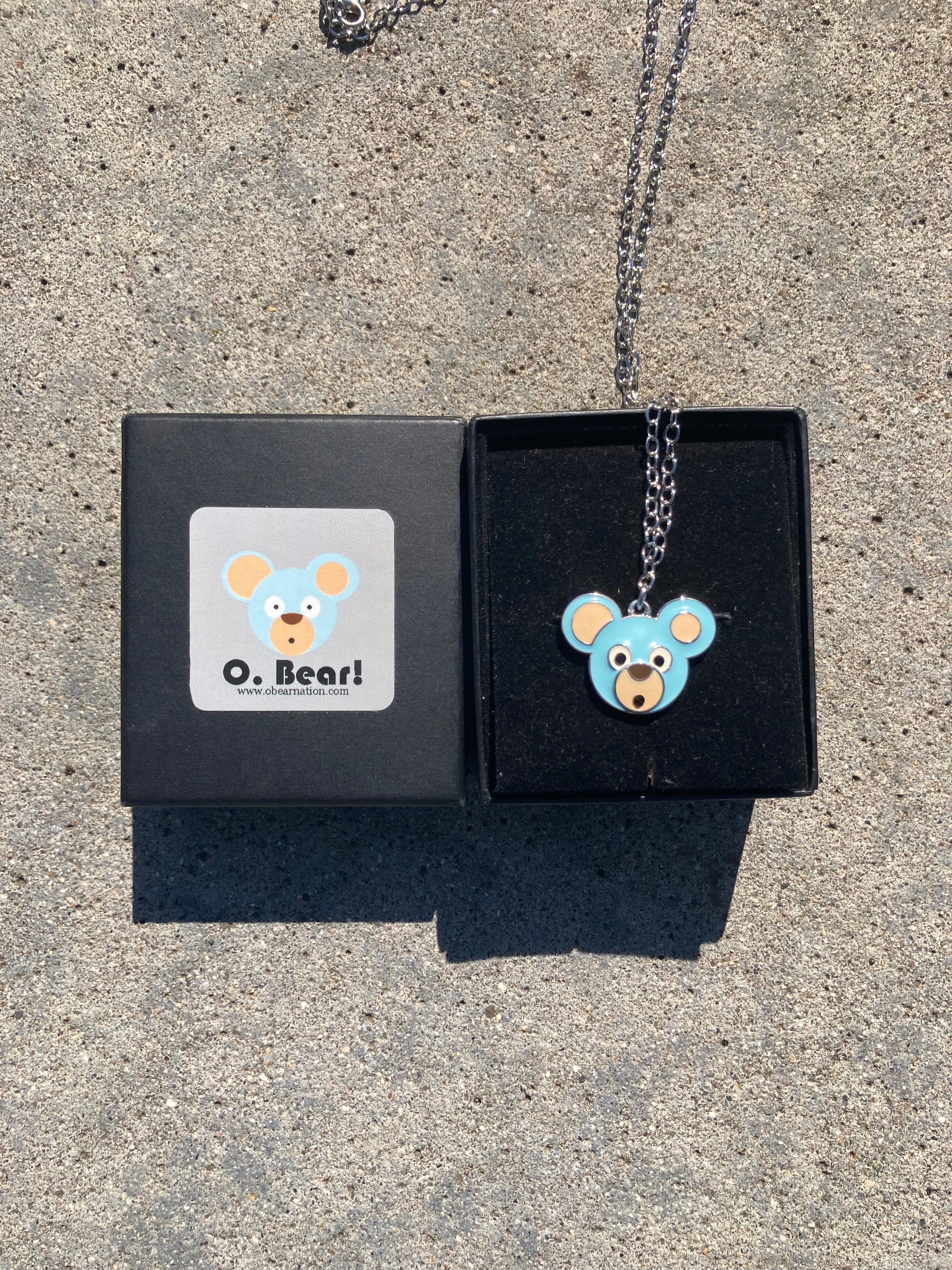 Necklace with an O. Bear pendant in a black box on a concrete surface