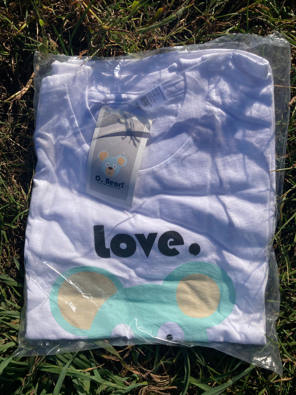 White t-shirt with 'love, O. Bear' printed on it, lying on grass