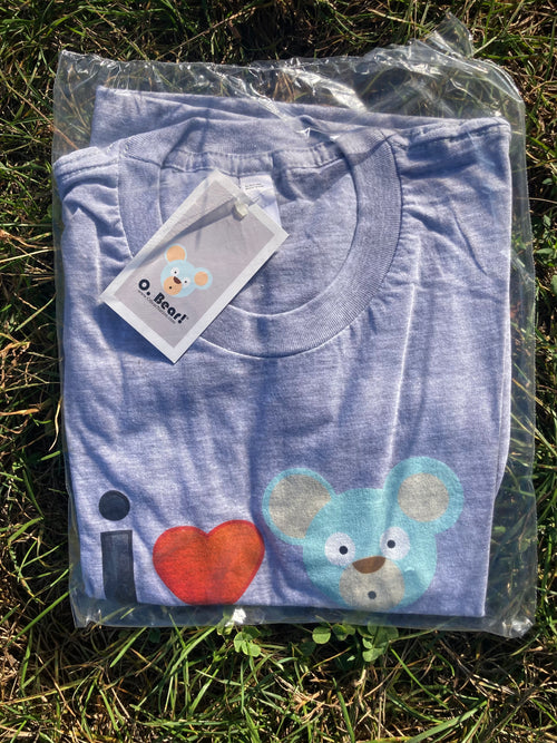 Folded grey t-shirt with a bear design and 'I love heart OBear O. Bear' text, still in packaging on grass.