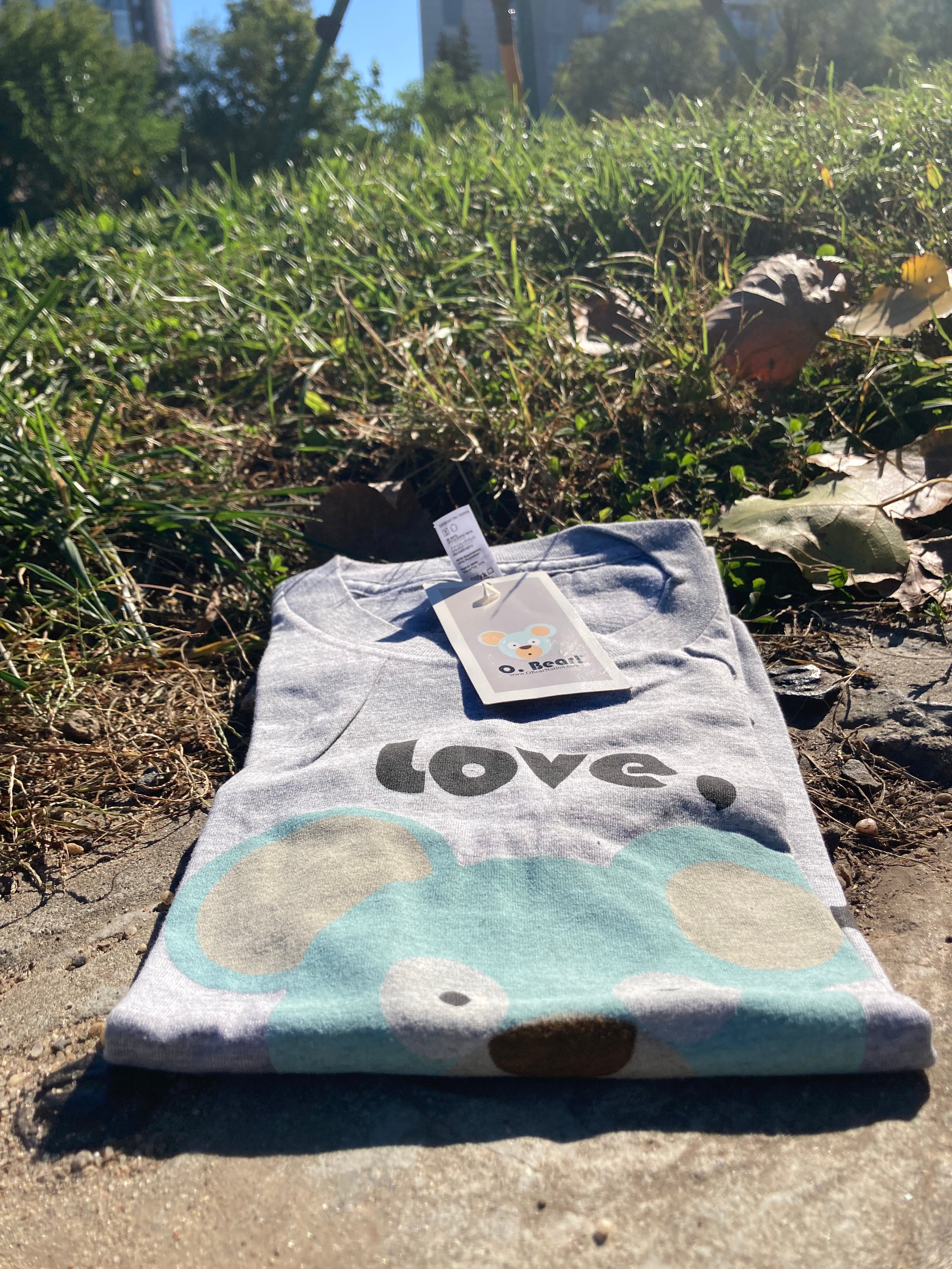 Folded t-shirt with 'Love, O. Bear!' text and cloud pattern on grass